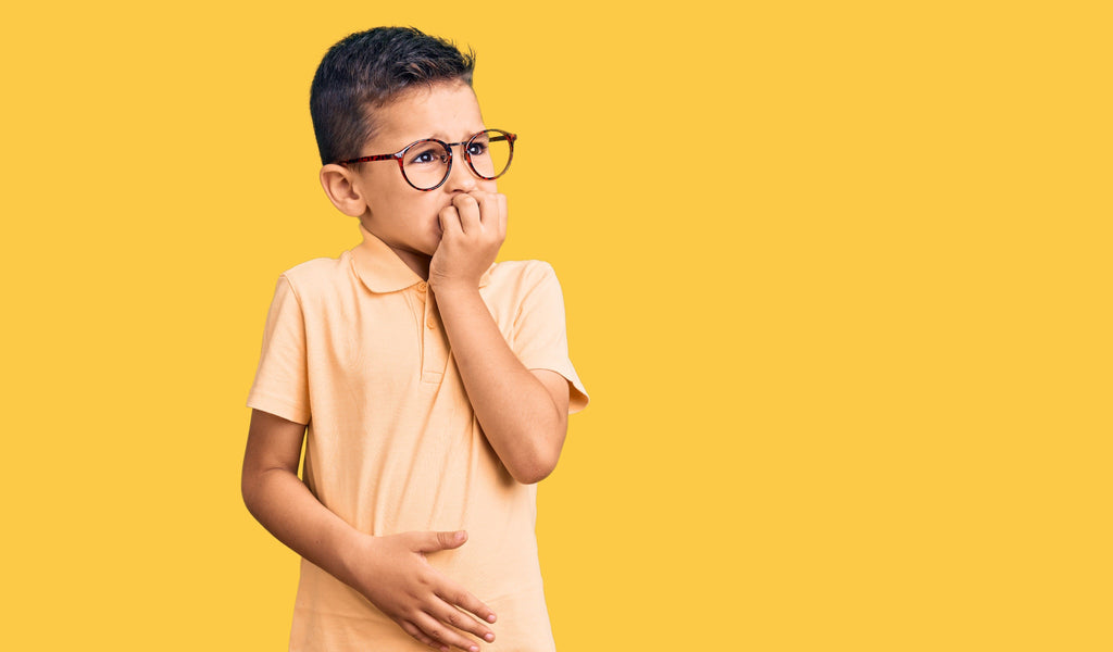 Little boy wearing glasses bites his nails as he deals with sensory overload anxiety.