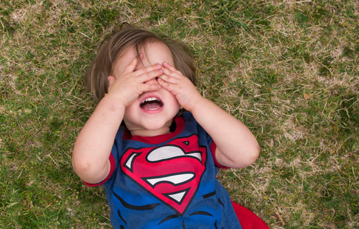 Little boy dressed as superhero has a meltdown on grass with hands over eyes. Meltowns in kids with autism can be common.