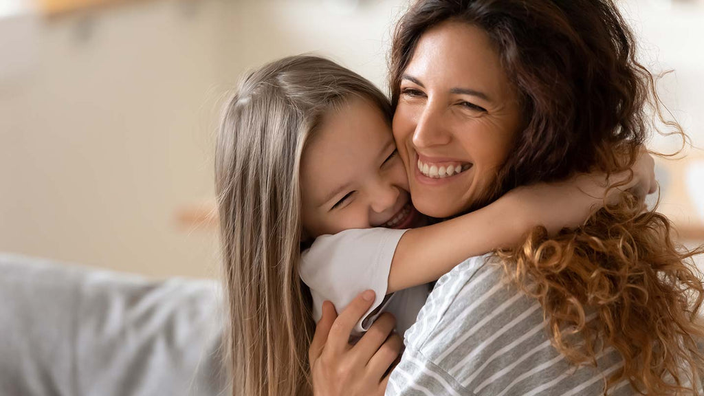 Smiling mother cuddles and hugs excited daughter with autism.