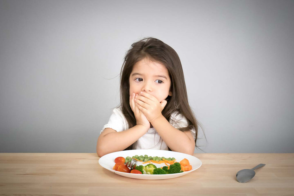 Little girl at table with hand over her mouth because she has picky eating habits or ARFID.