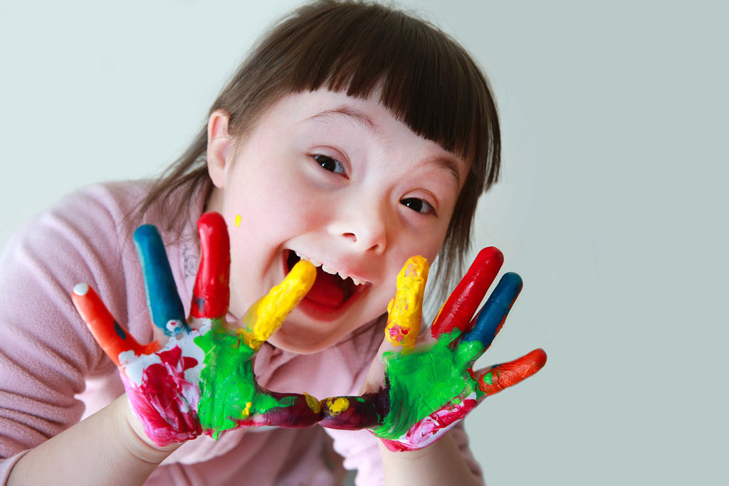 Smiling little girl with mosaic down syndrome playing with finger paints