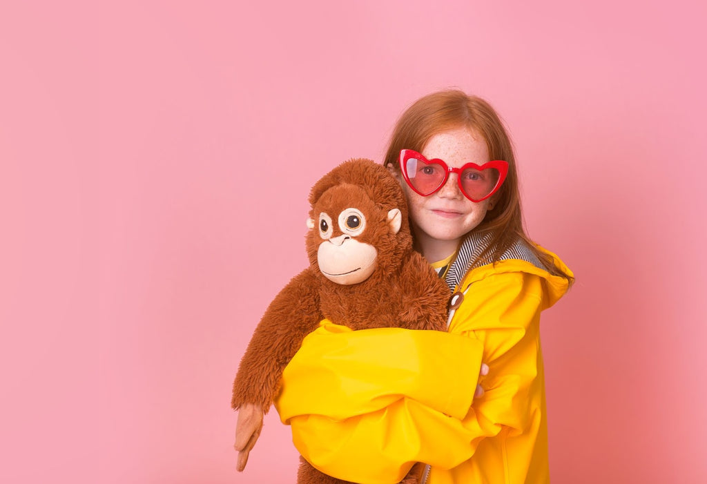 Little girl in yellow jacket and red sunglasses holds a weighted stuffed animal.