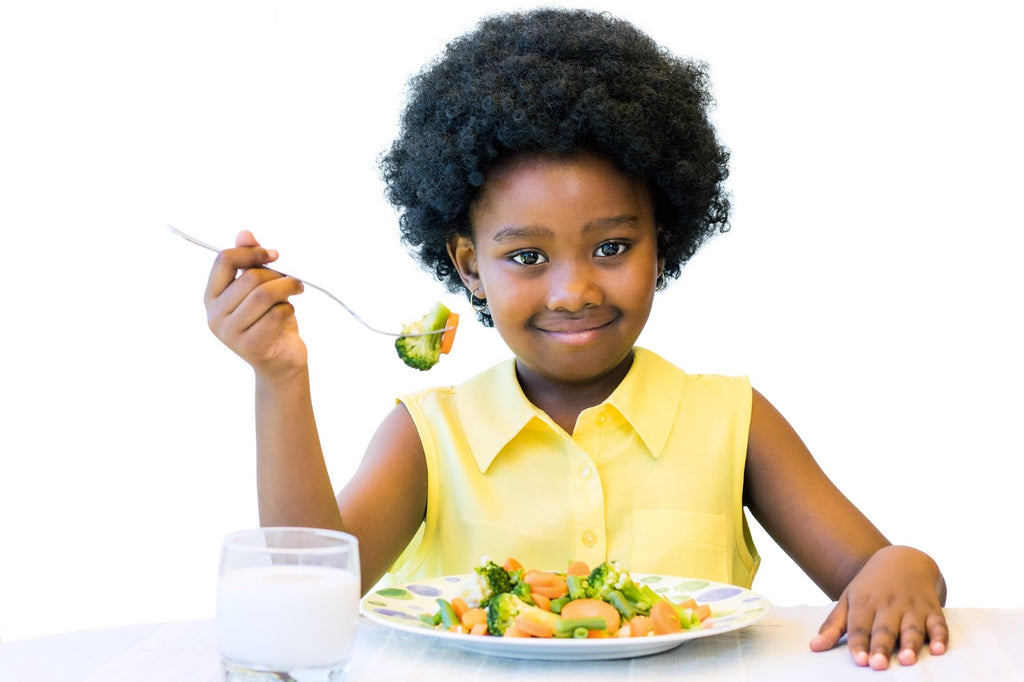 Young girl smiles as she prepares to eat a plate of veggies in front of her.