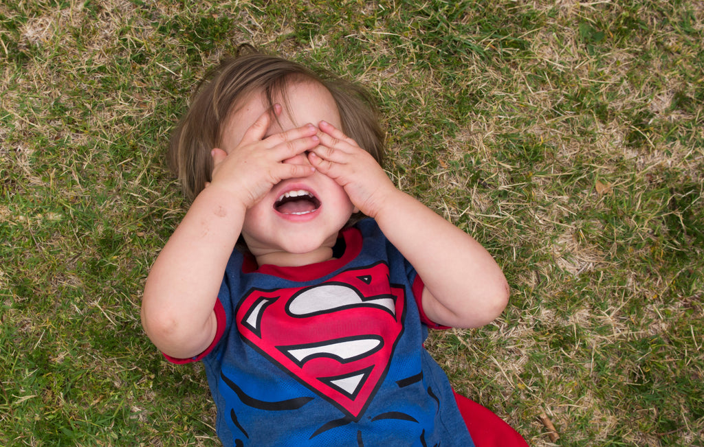 Little boy dressed as superhero has a meltdown on grass with hands over eyes. Meltowns in kids with autism can be common. 