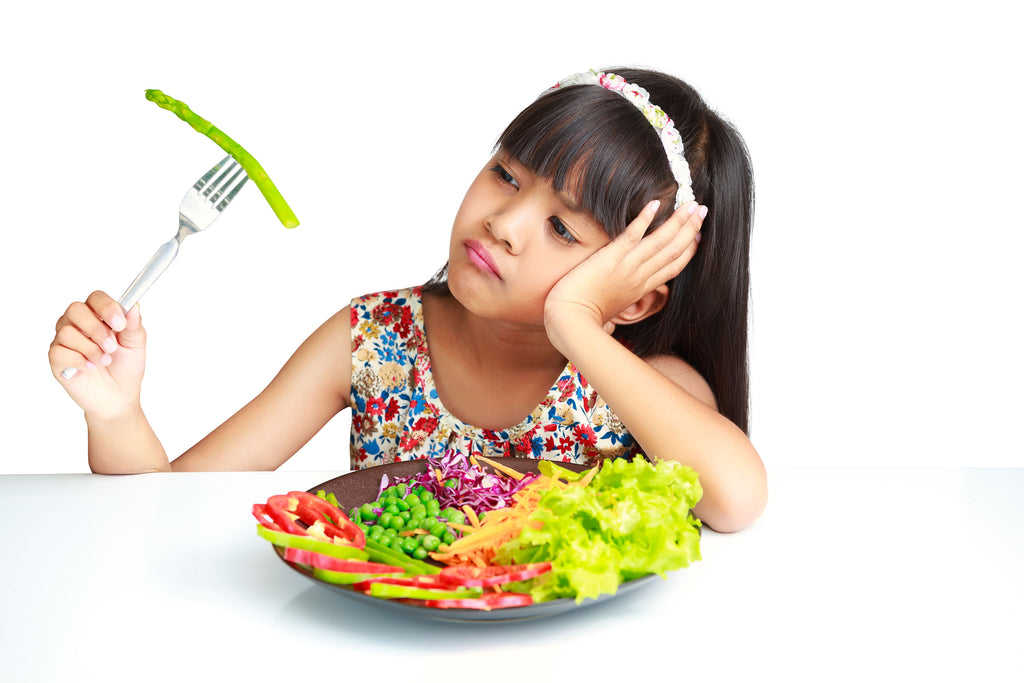 Little girl looking at plate of folate-rich vegetables with disgust.
