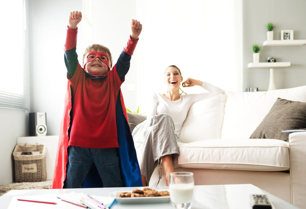 A little boy celebrating the autism strengths that make him shine by throwing hands in the air while wearing a superhero costume.